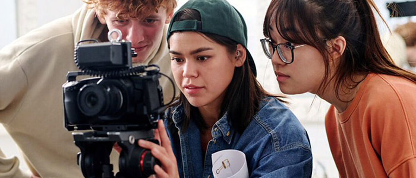 Three students with a DSLR on a tripod shooting a video. They are consulting with each other and checking the framing of the shot.