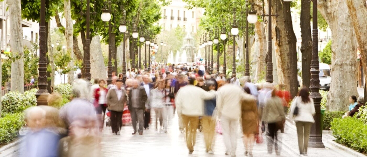 Crowds of people walking down a busy tree-lined street