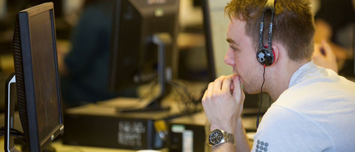 Student sitting at computer watching the screen and listening to headphones