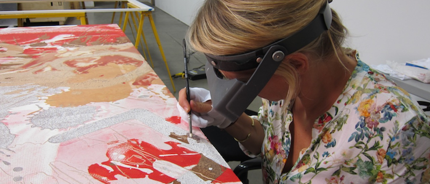 A woman wearing goggles and holding a paintbrush as she carries out conservation work on a contemporary painting.