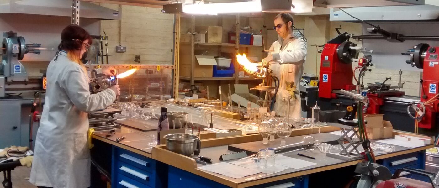 Two glassblowers in glassblowing workshop working on different pieces of glassware