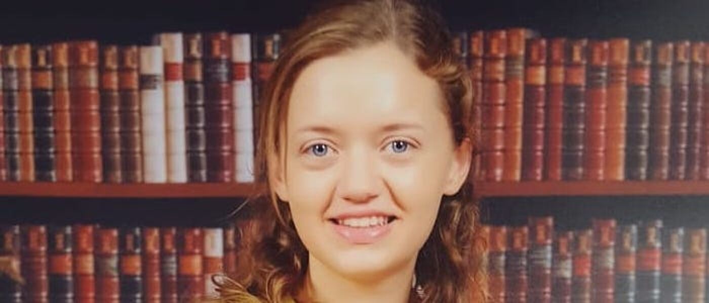 Female graduate in front of book case