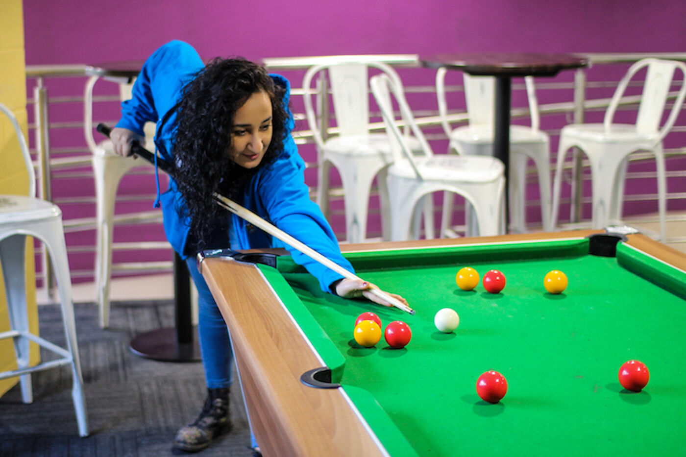 A female Residence Life Assistant in a blue hoodie playing pool