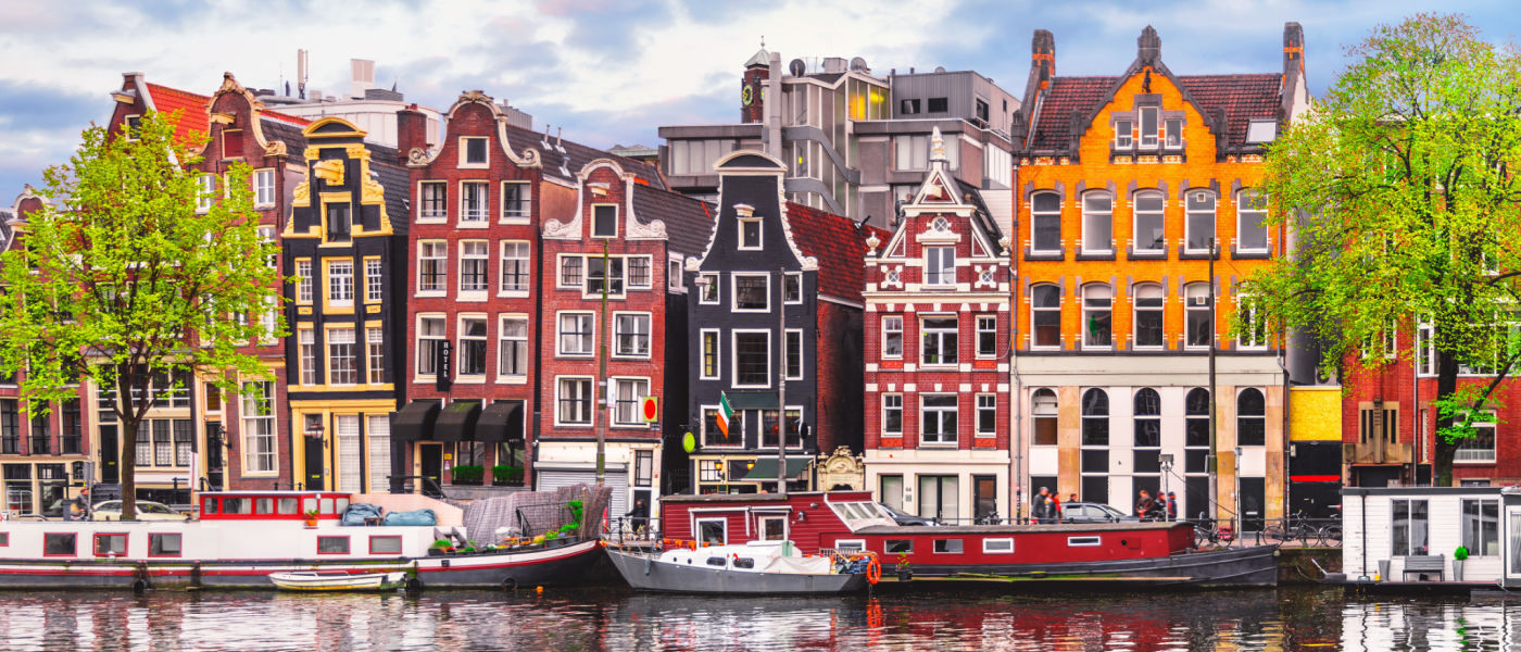 Row of narrow houses overlooking the Amstel River in Amsterdam, with houseboats in the foreground [Photo: Shutterstock]
