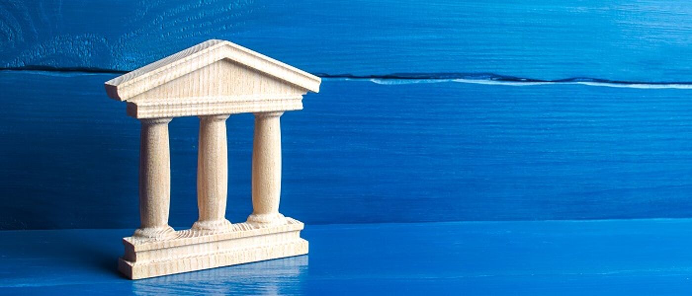 Small wooden model of gov building with pillars on bright blue background