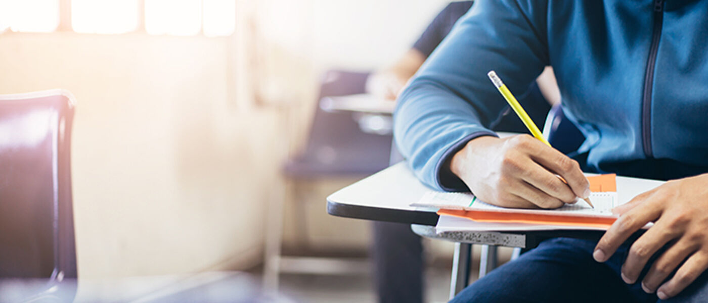 soft focus.high school or university student holding pencil writing on paper answer sheet.sitting on lecture chair taking final exam attending in examination room or classroom.student in uniform
