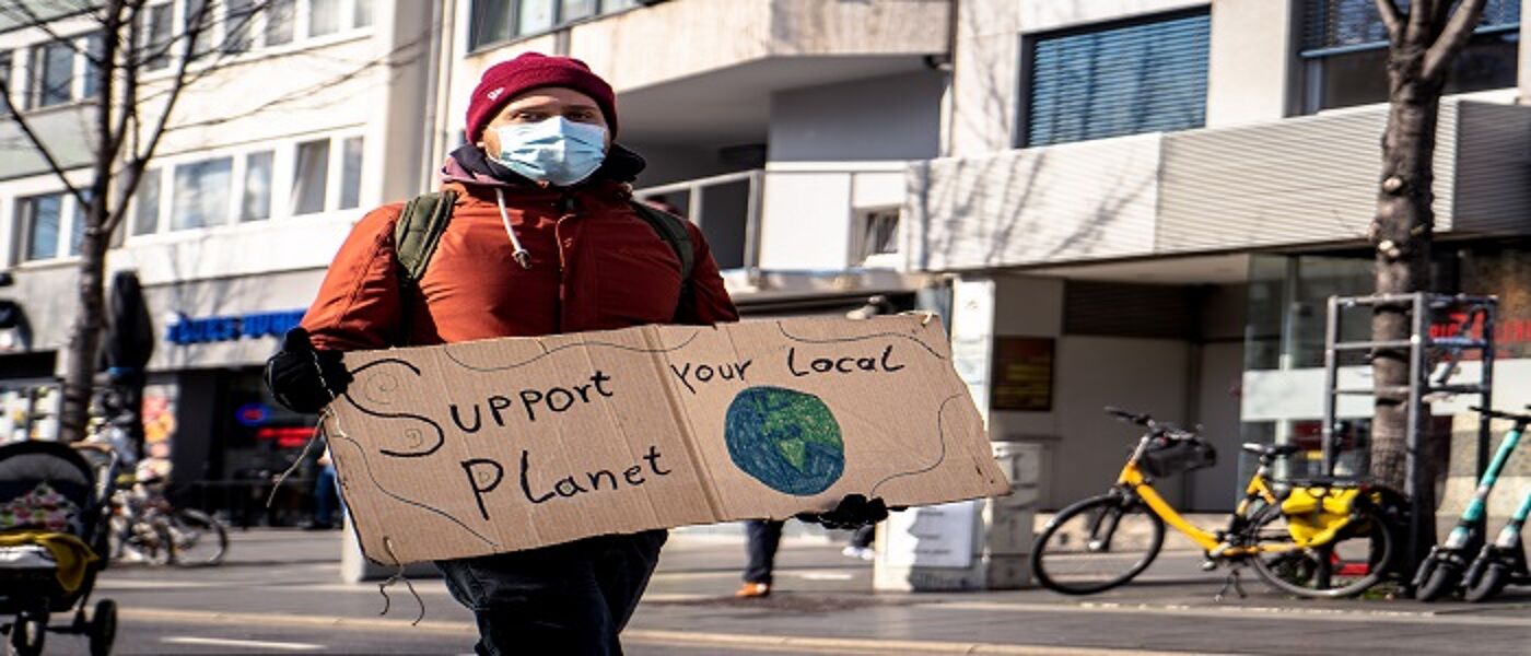 Protestor in mask holding a sign 'Save your local planet'