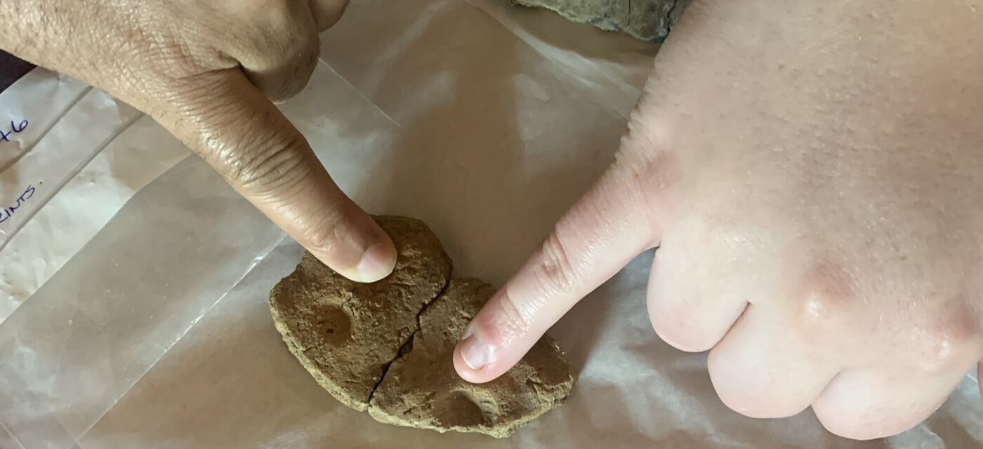 Two people touching indentations on a small piece of pottery with their little fingers