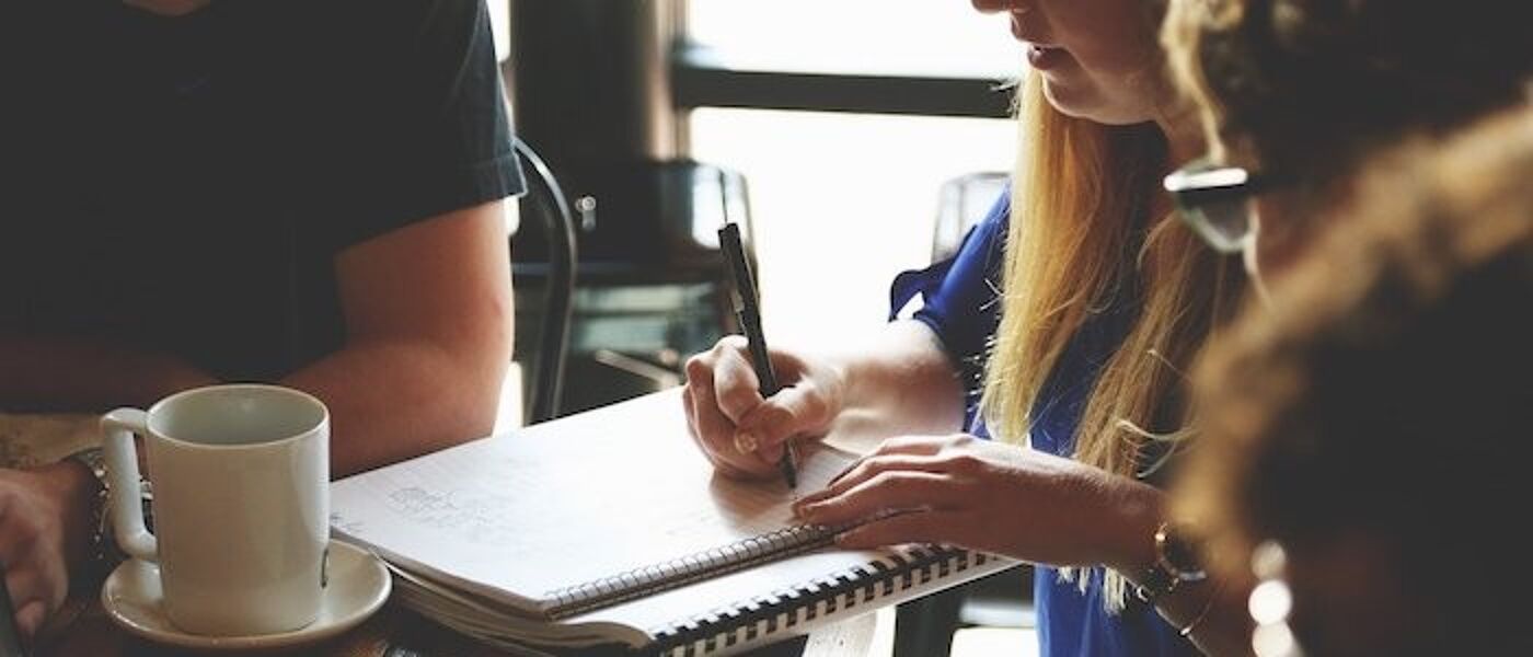 Image of people sitting at a desk brainstorming with note pads and laptop