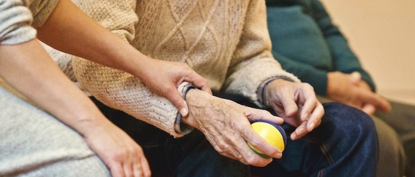 Image of an elderly man using a ball to exercise with a younger person by his side