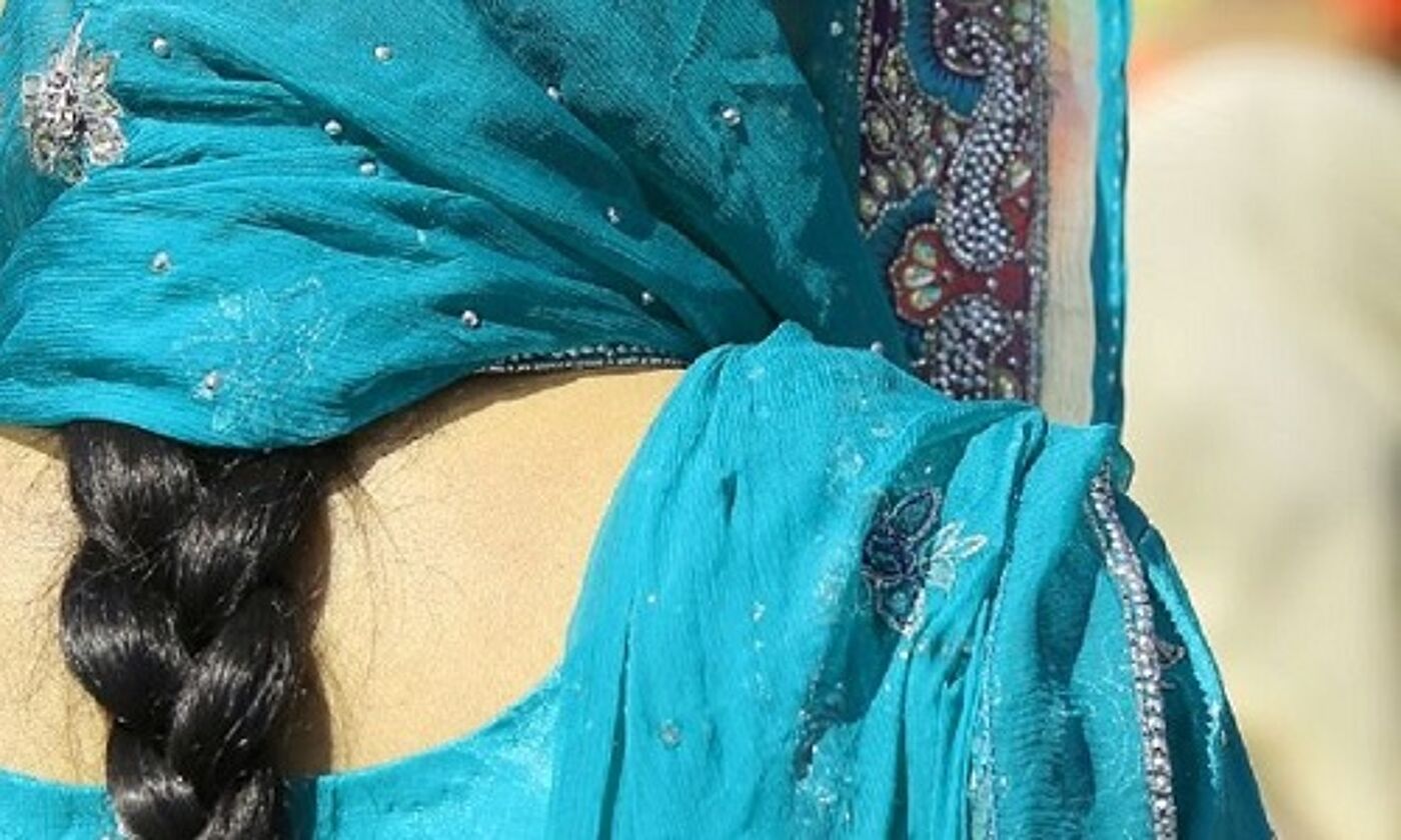 Back view of an Indian woman with her black hair in a plait and wearing in a light blue outfit and scarf over her head. Image credit: ChiccoDodiFC | iStockphoto https://www.istockphoto.com/photo/woman-with-dress-and-long-black-hair-gm954544102-260615928