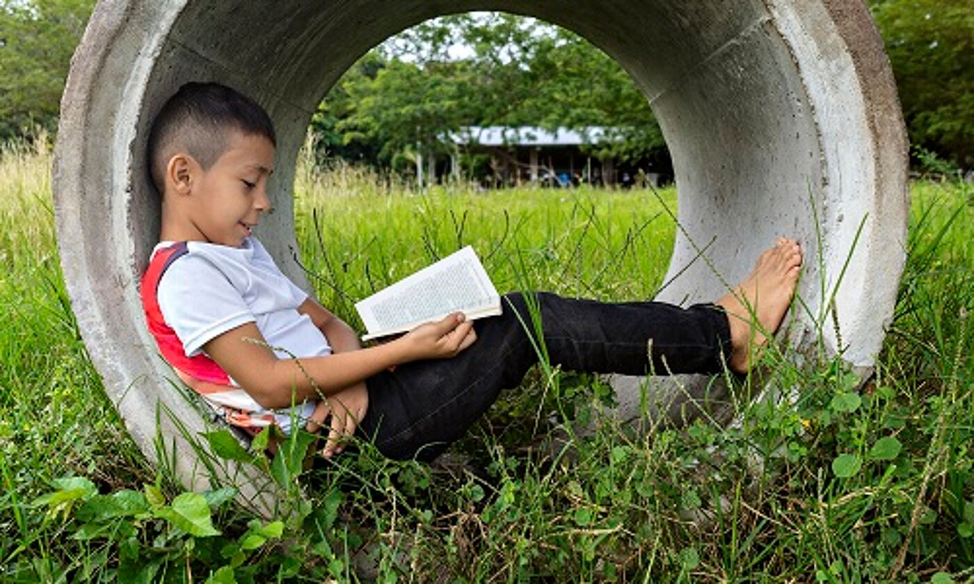 A boy lying inside a concrete pipe in a field and reading a book. Image credit: RECVISUAL | iStockphoto https://www.istockphoto.com/photo/boy-reading-a-book-sitting-on-a-concrete-pipe-on-a-sidewalk-very-happy-and-smiling-gm1295650597-389311729