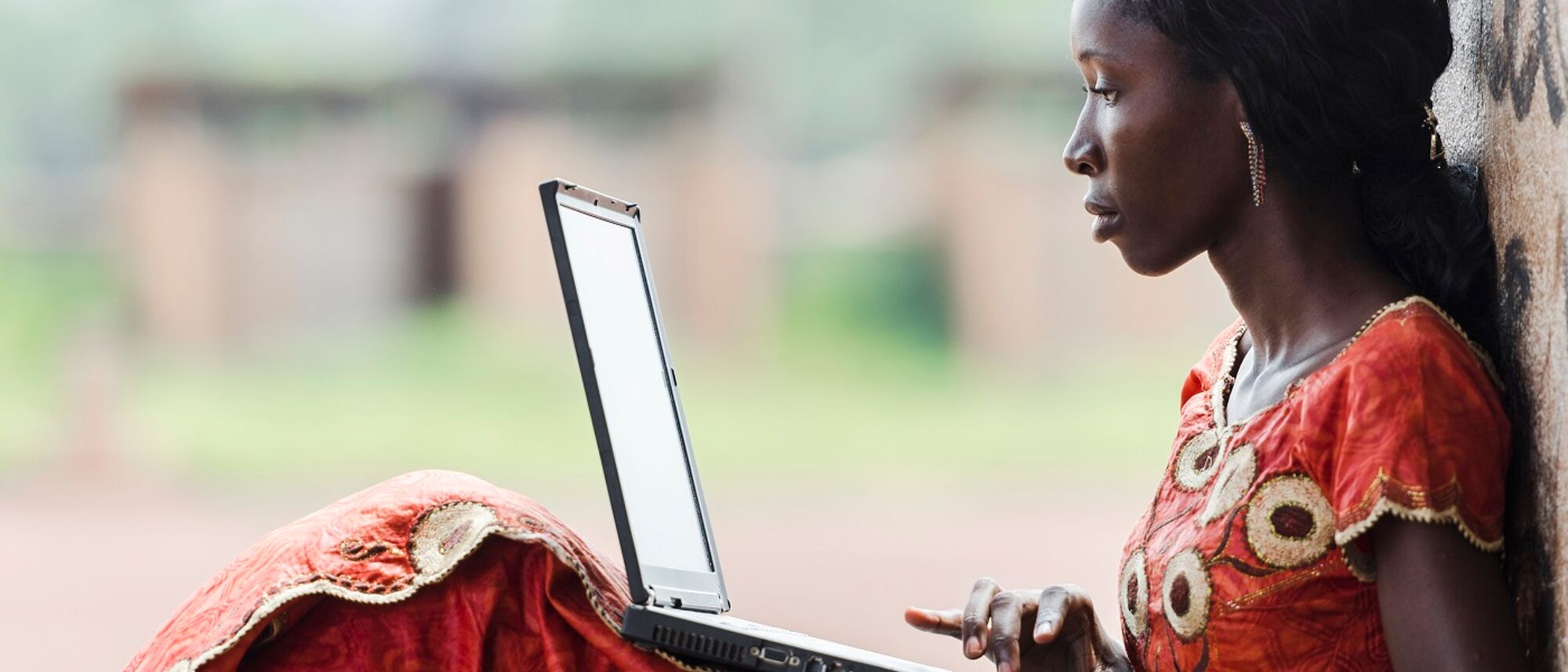 A young African woman sitting and leaning against a wall to use her laptop.Image credit: borgogniels | iStockphoto https://www.istockphoto.com/photo/technology-symbol-african-woman-studying-learning-lesson-gm529835071-54284780