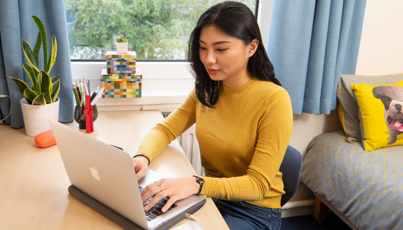 A student in her residence sat at a desk typing on a laptop