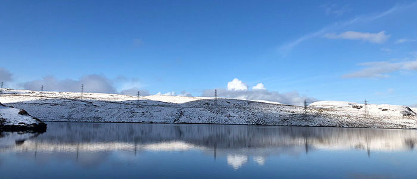 clear blue sky over a snowy strip of land above a smooth reflective lake surface