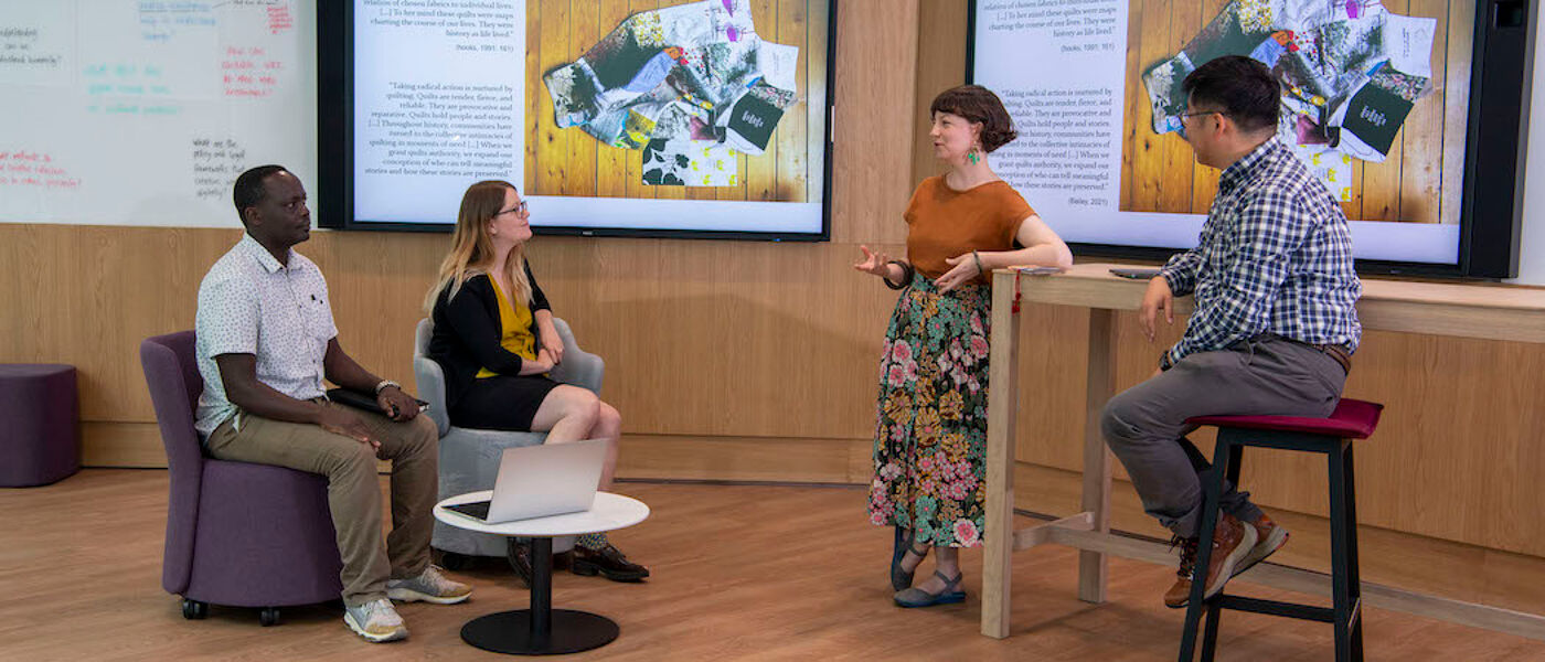 People in a discussion in modern room with large screens. Three are sitting ate one woman is standing, leaning on a high desk as she talks. Source: GU Image Library, ARC research collaboration 011.JPG