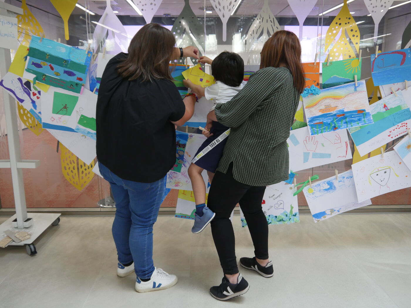Three people looking at collection of artworks of rivers hanging from clothes line