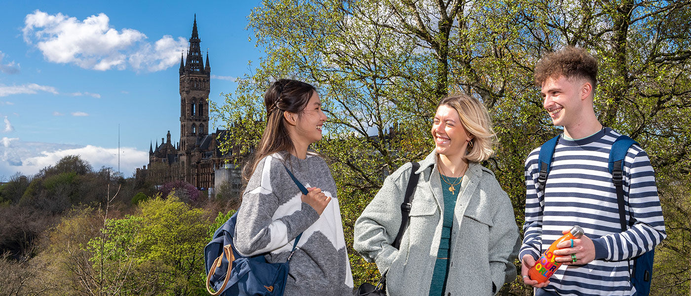 Three students talking with the University Tower in the background