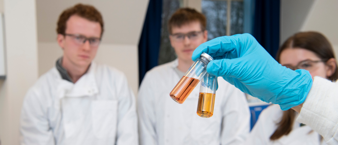 Students in a lab with a gloved hand showing two vials