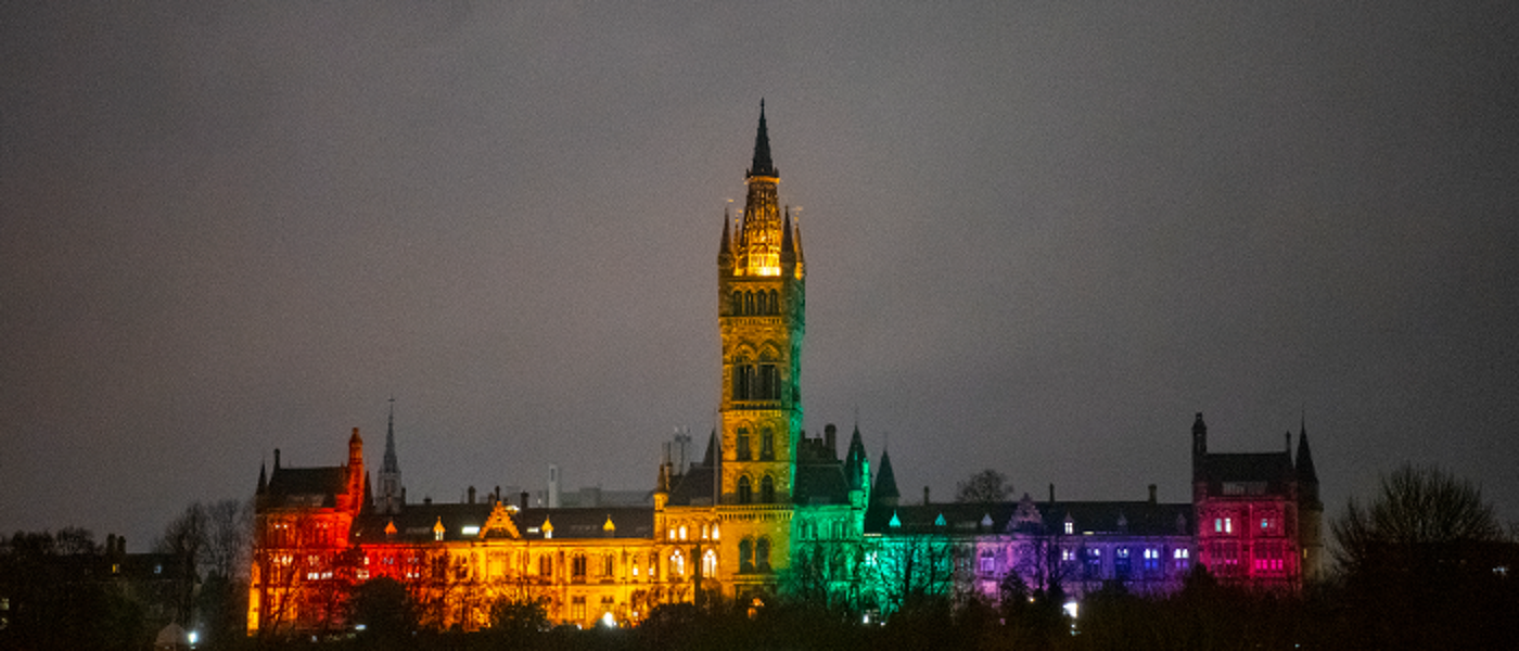 A wide photograph of the university of glasgow at night with the lights turned into a rainbow pattern to signify the Pride Flag