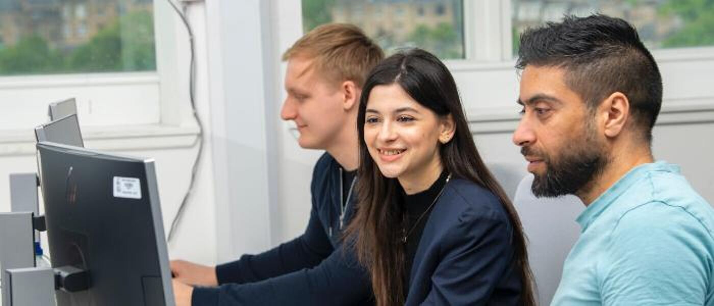 Three computing students sitting in a row looking at screens