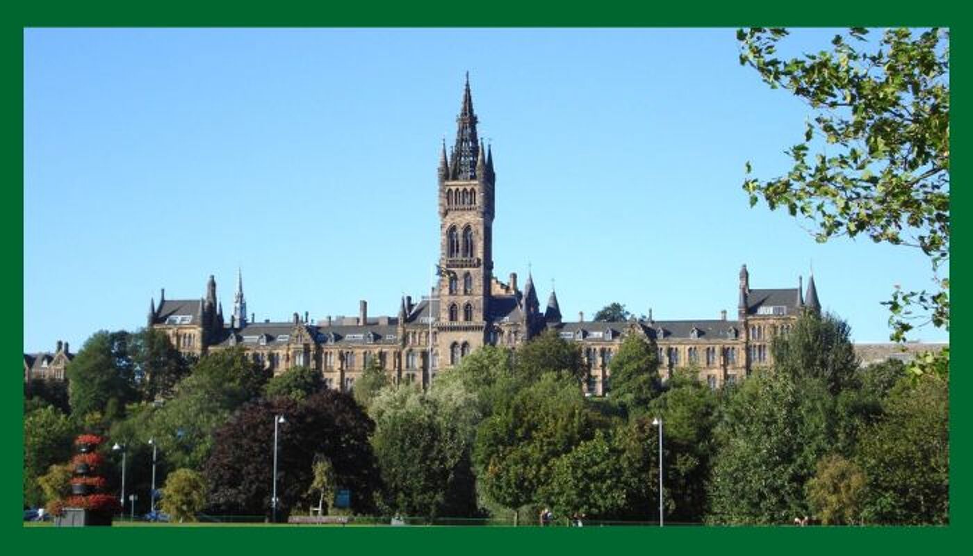University tower from a distance with green grass and trees at the forefront