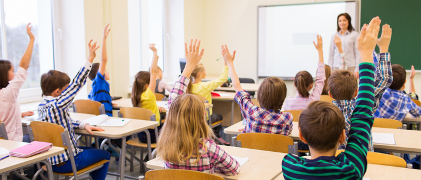 Students sitting in classroom with hands raised