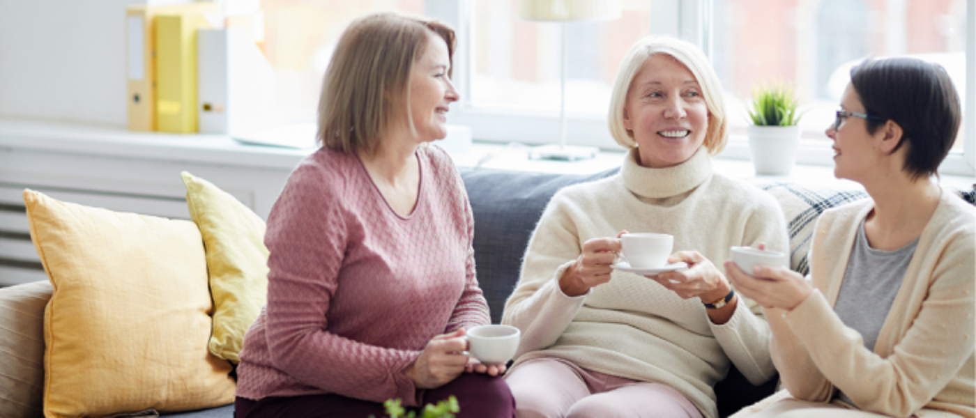 Three women sitting on a sofa with cups of tea chatting