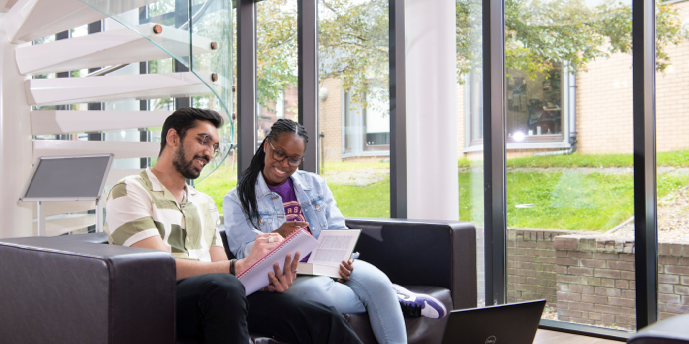Two students sitting on a sofa laughing and studying in the library