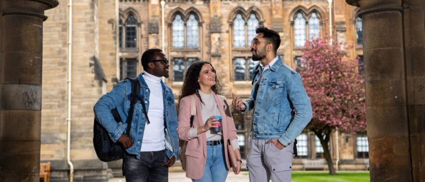 Group of three students chatting in the West Quadrangle in the main building