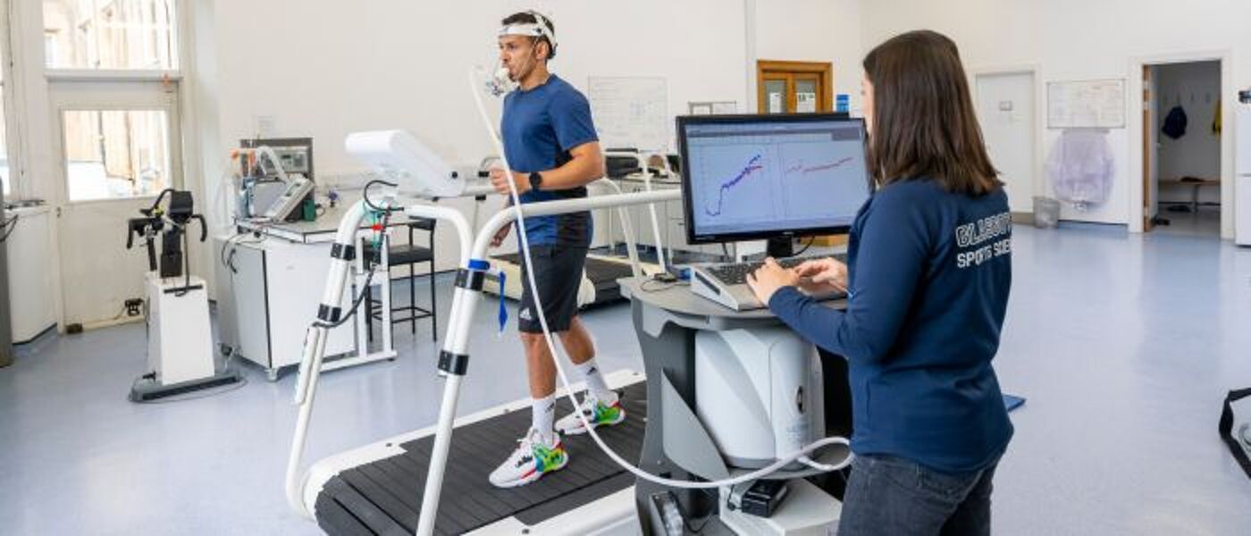 A man running on a treadmill with a researcher monitoring respiration with equipment in the sports science lab